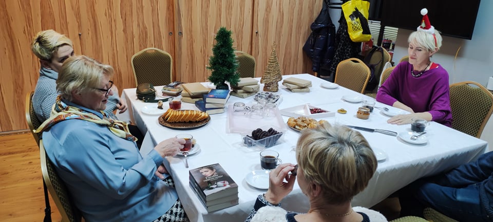 na zdjęciu cztery kobiety siedzące przy stole. Na stole dekoracje śwąteczne, casto oraz książki