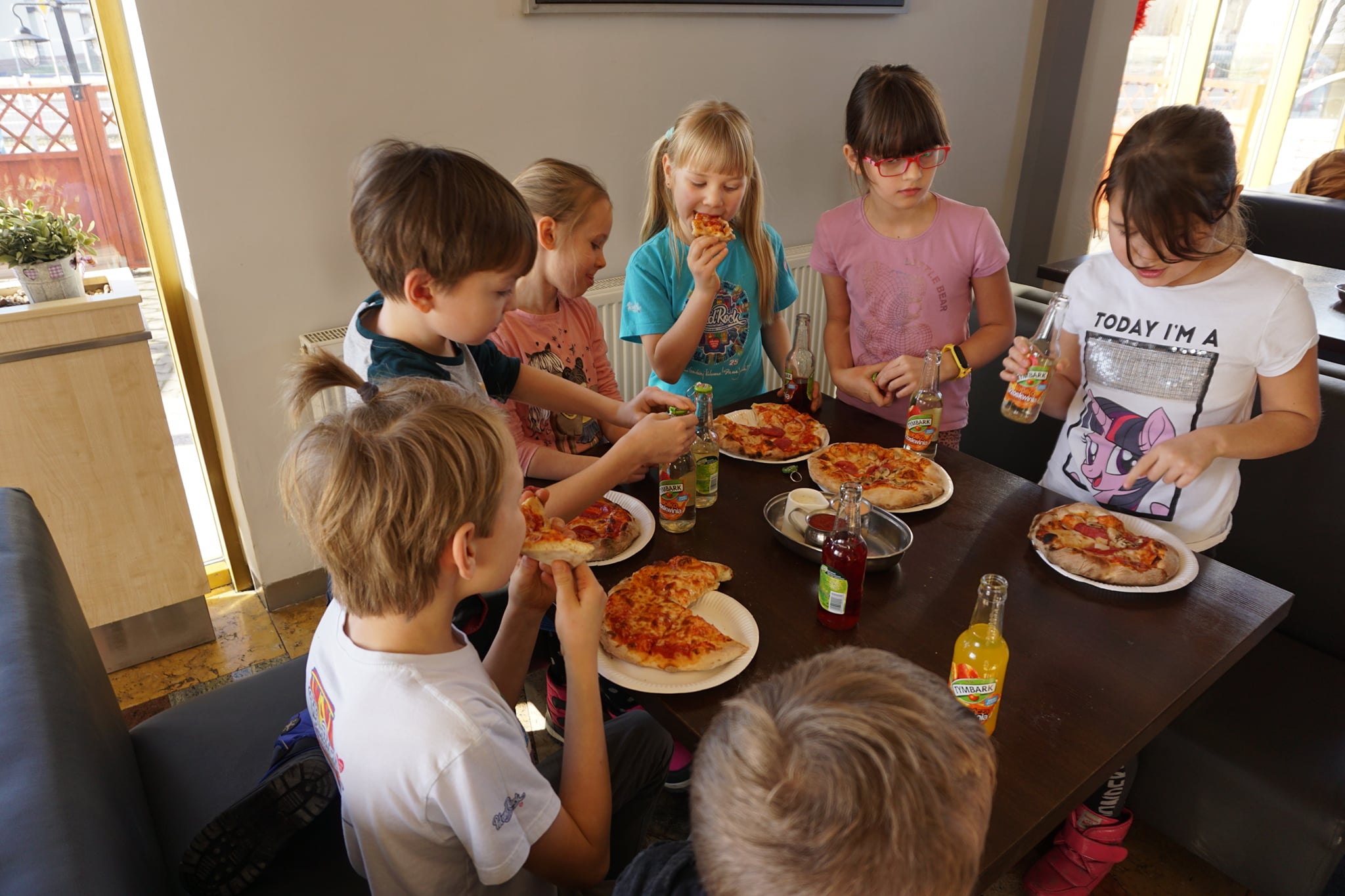 Dzieci przy stole z talerzami pizzy i sokiem