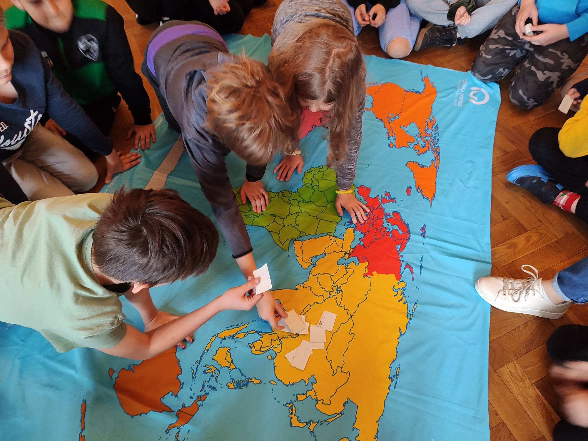 trójka dzieci nachyla się nad mapą świata