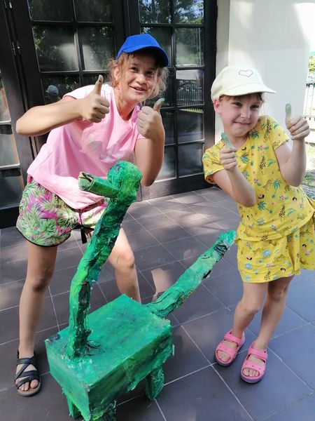 dwie dziewczynki stojące przy kartonowym dinozaurze 