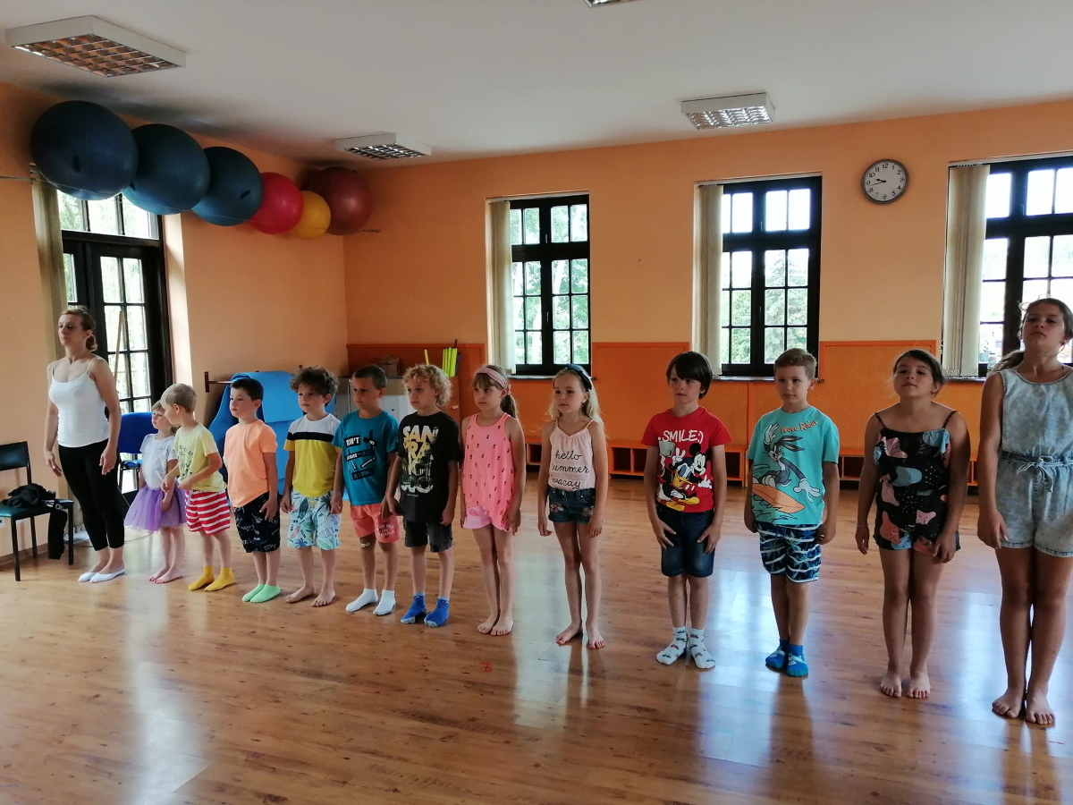 Grupa dzieci, chłopcy i dziewczynki stojący w lini prostej na sali gimnastycznej