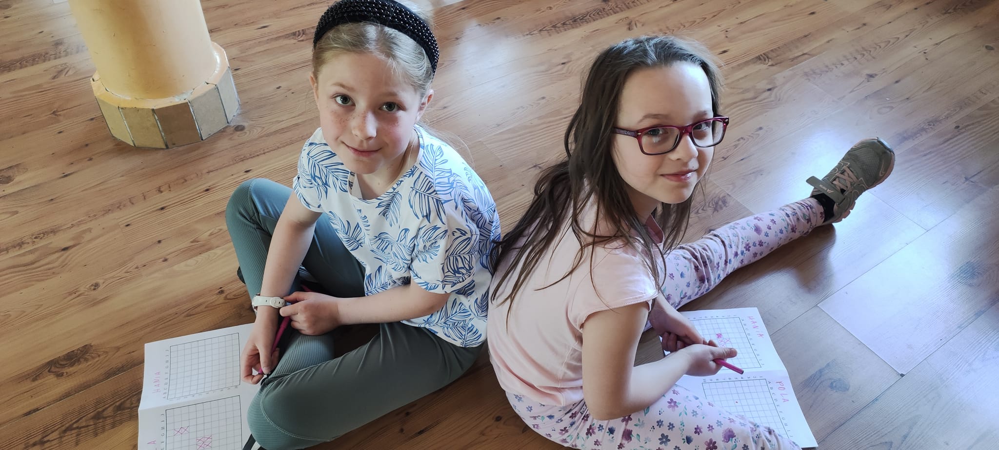 Dwie dziewczynki siedzą na podłodze a przed nimi kartki papieru