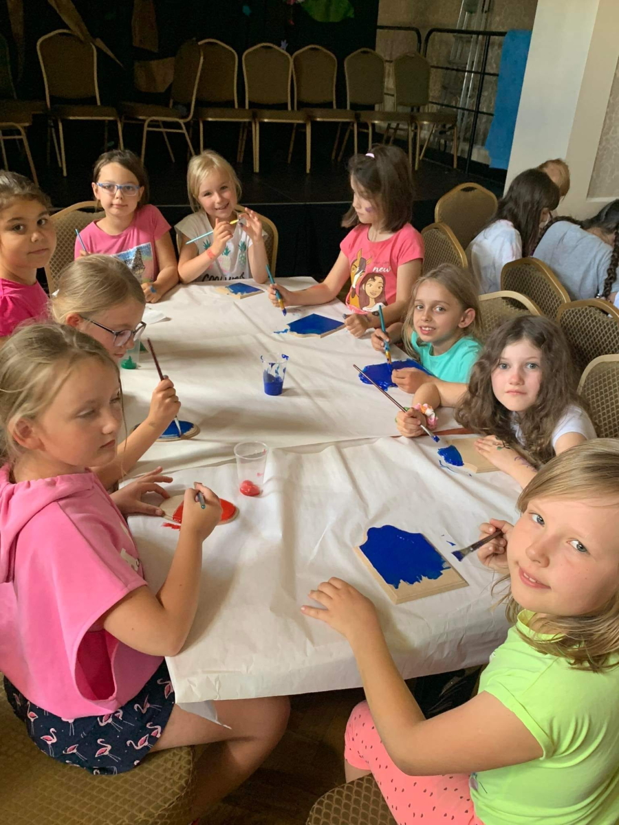 Grupa dziewczynek siedząca przy stole. Dzieci kolorują na niebiesko kuchenne deski