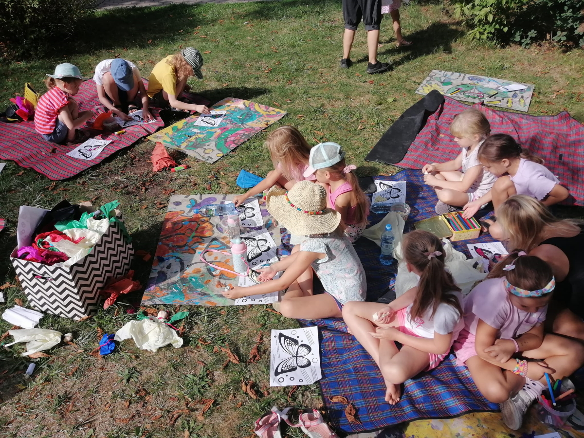 dzieci siedzące na kocach na trawie, tworzą pracę z bibuły