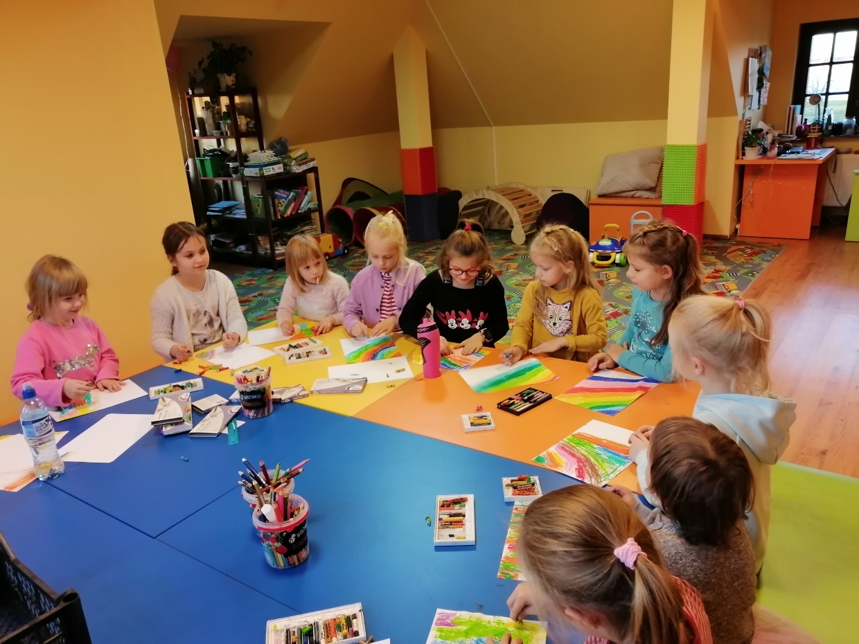 grupa dziewczynek siedzi przy stoliku. dziewczynki kolorują