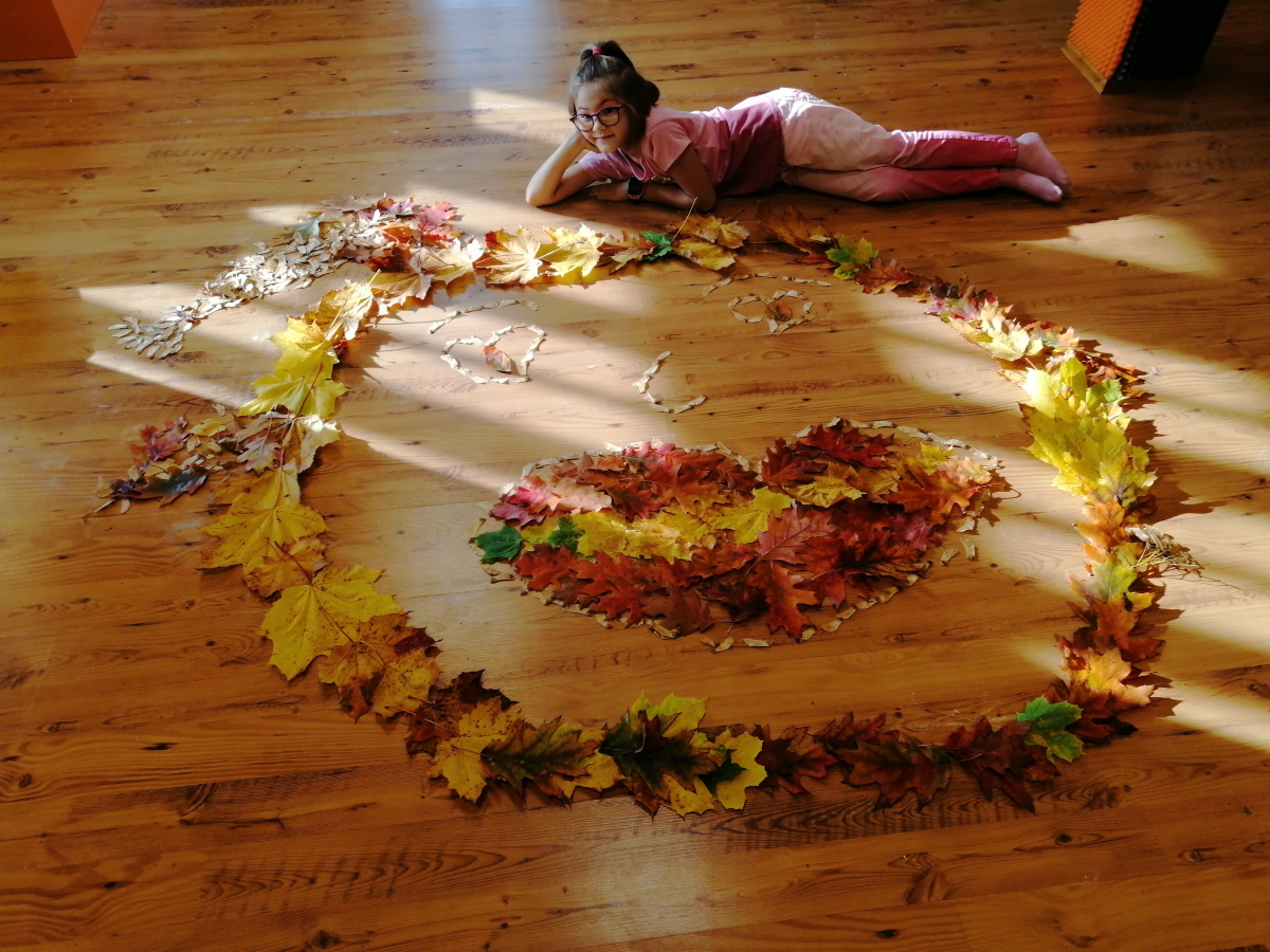 dziewczynka leży przy stworzonej przez siebie mandali z liści 