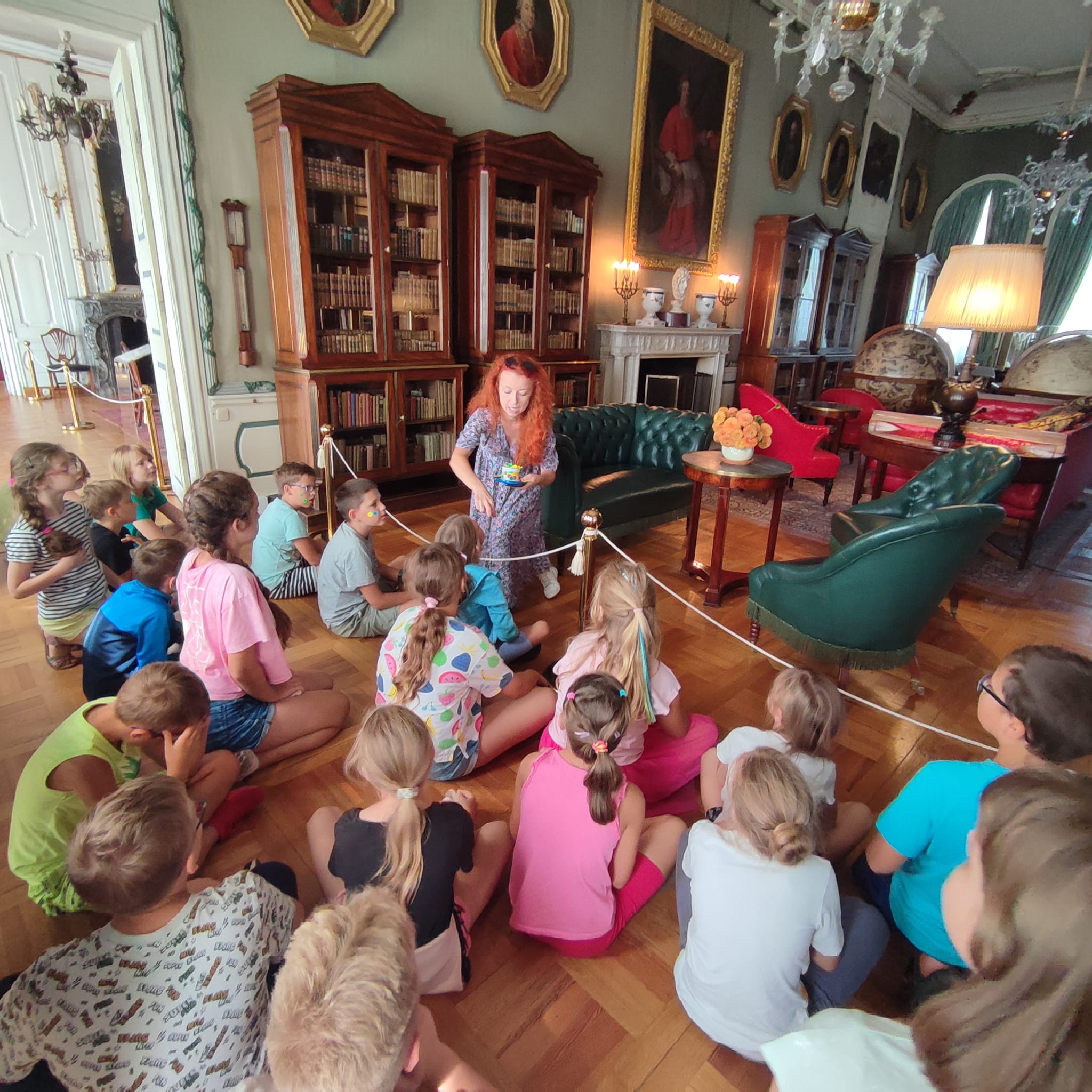 Grupa dzieci siedzi na podłodze i słucha opowieści przewodniczki, pałac Nieborów