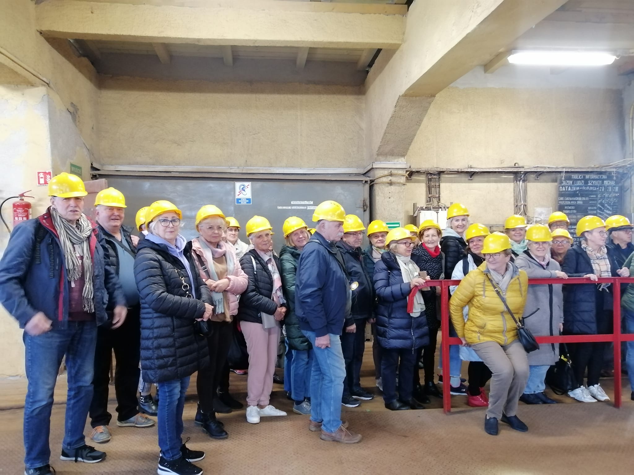 Grupa seniorów w oczekiwaniu na windę w kopalni soli w Kłodawie. Każdy ma żółty kask na głowie